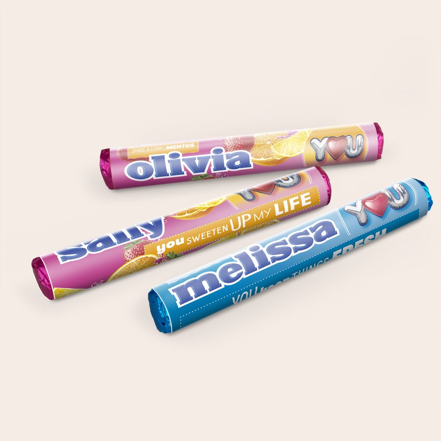 Three personalized Mentos rolls, two pink with fruit designs and names "Olivia" and "Samy," one blue with "Melissa" and "YOU SWEETEN UP MY LIFE" printed on them.