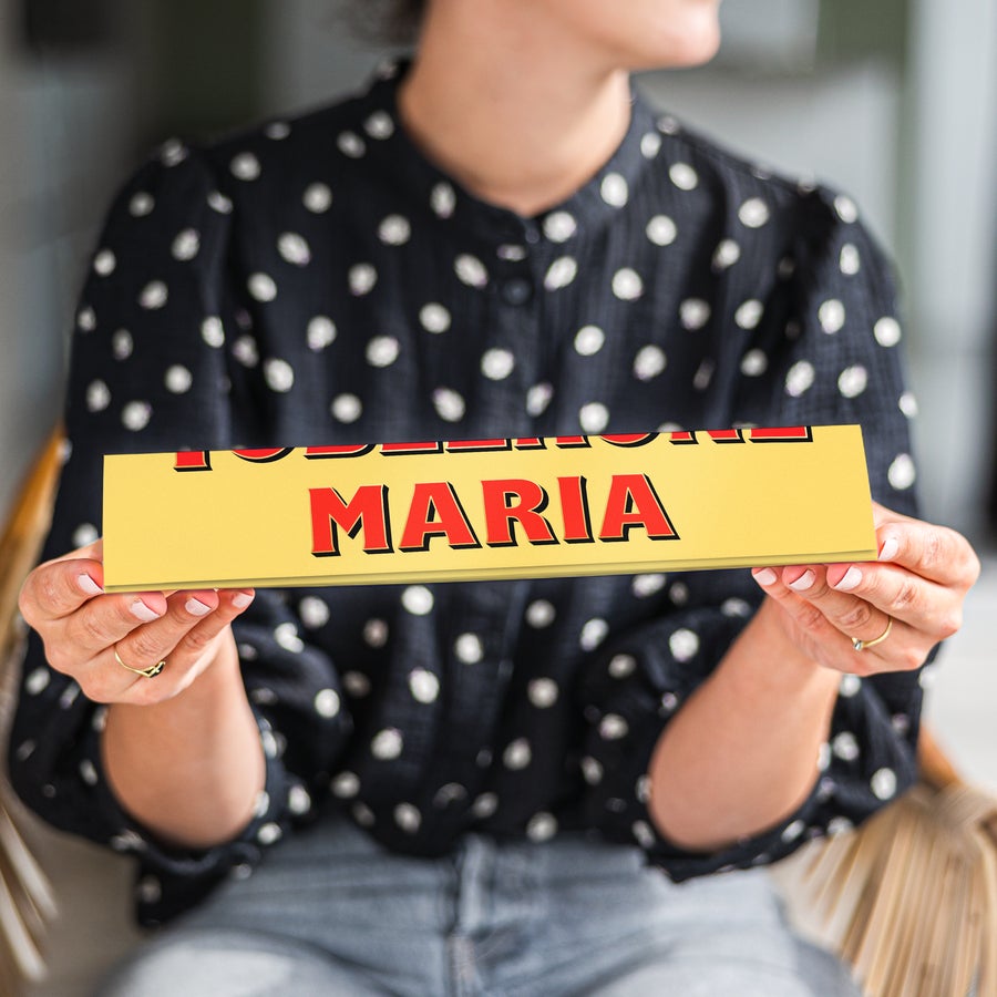 A person holding a personalized large Toblerone bar wrapper with the name MARIA printed in red.